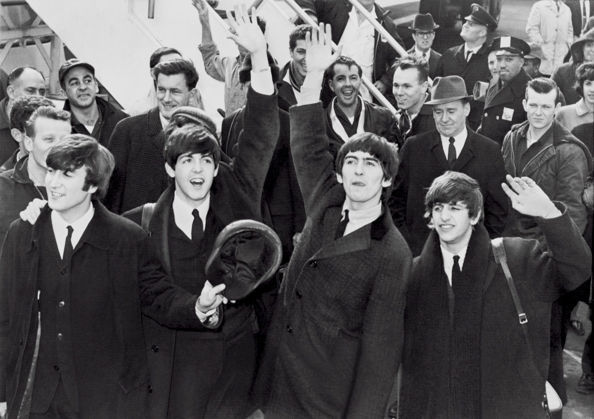 The Beatles, famous musicians stepping off a plane, waving to a crowd of admirers.