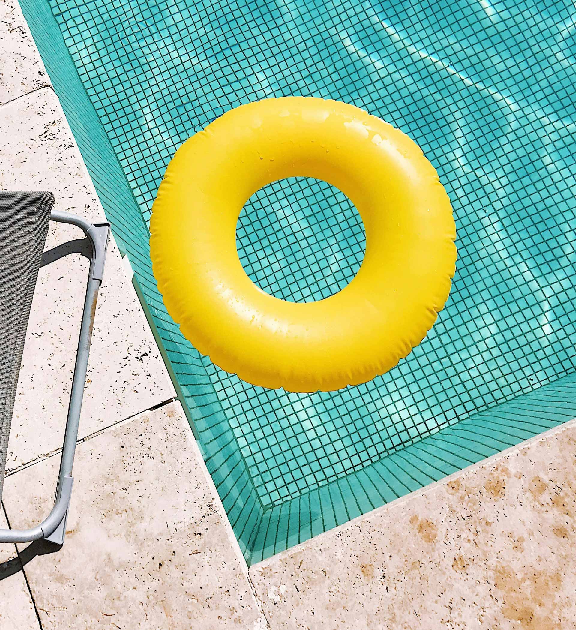 Bright yellow ring float on a pool & next to a chair.